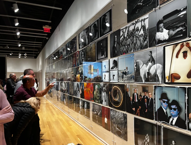 Person in art gallery points and looks at salon wall filled with photographs by Annie Leibovitz.